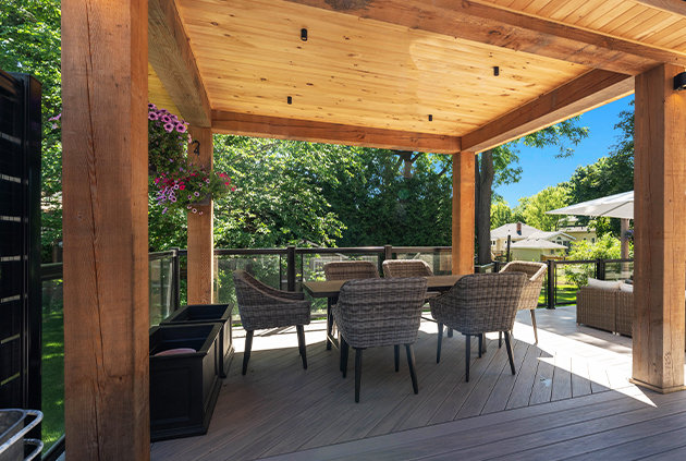 Backyard custom deck with a pavilion, outdoor furniture, and glass railing.